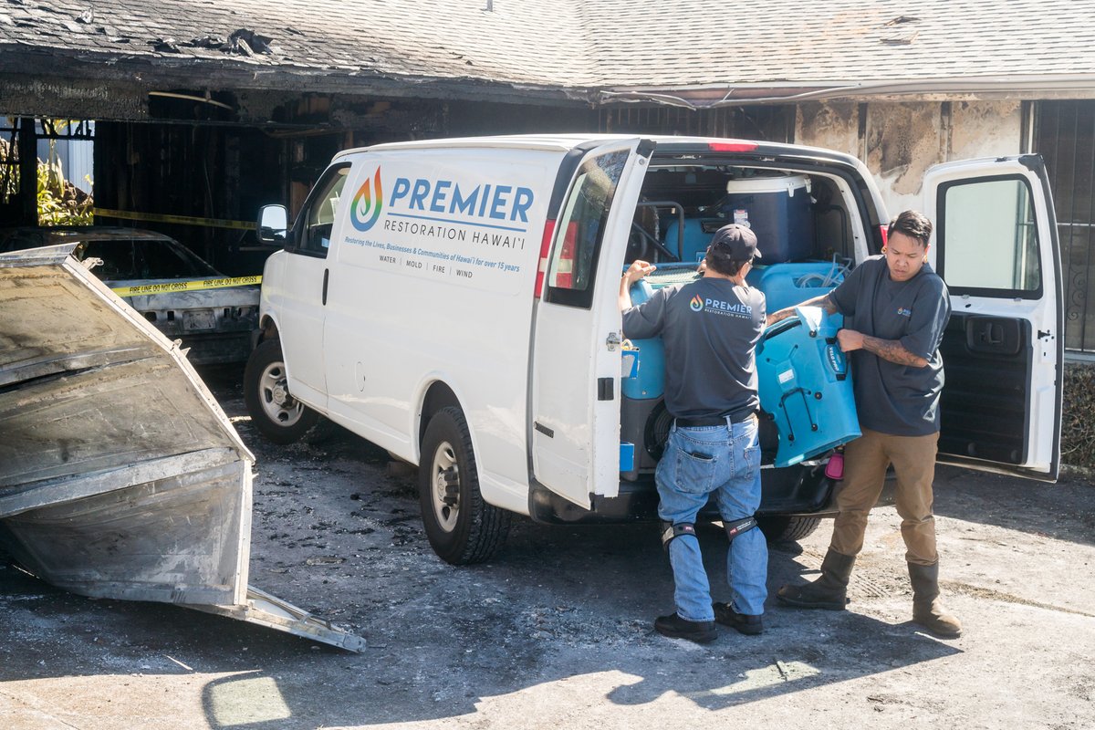 Restoration team unloading equipment from Premier Restoration Hawaii van at fire damage site.