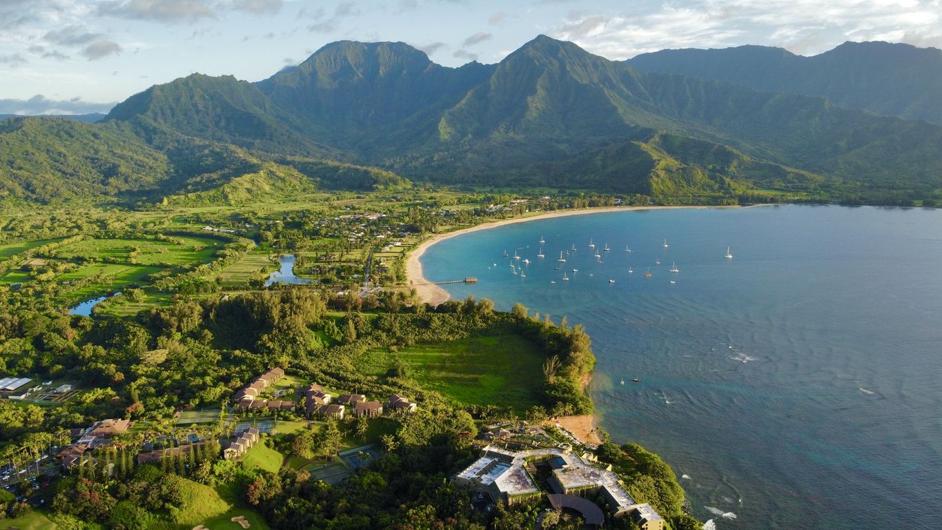 Aerial view of lush mountains and a scenic bay with sailboats in Hanalei, Kauai, Hawaii.
