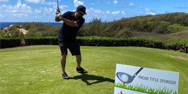 Golfer swinging a club on a sunny day at a course sponsored by Premier Restoration Hawaii.