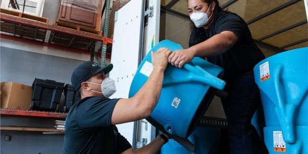 Two people wearing masks loading blue equipment into a truck.