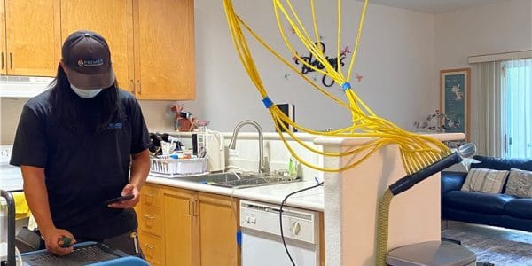 A worker using drying equipment after water damage in a kitchen setting.