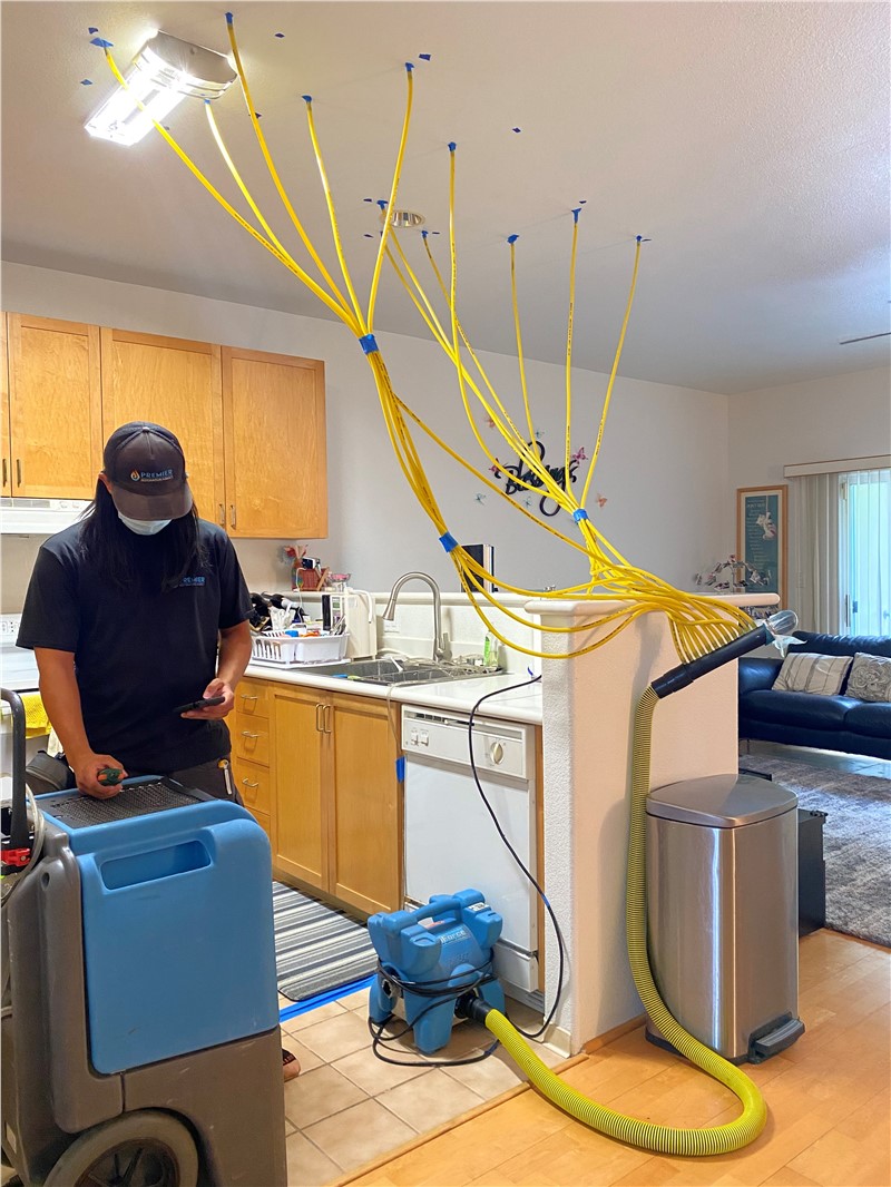 A worker using drying equipment after water damage in a kitchen setting.