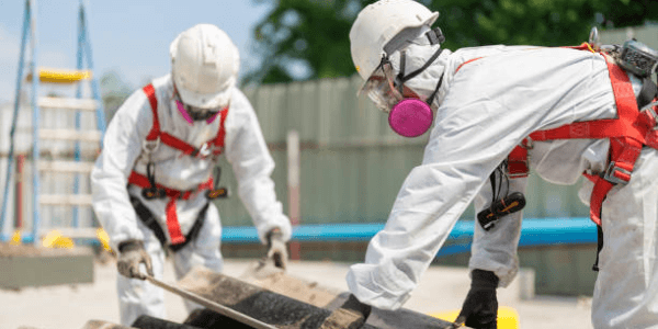 Workers in protective gear removing asbestos roof panels.