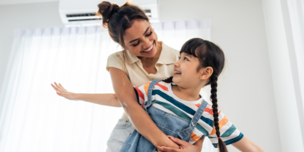 Mother and daughter smiling and hugging in a bright room with sunlight.