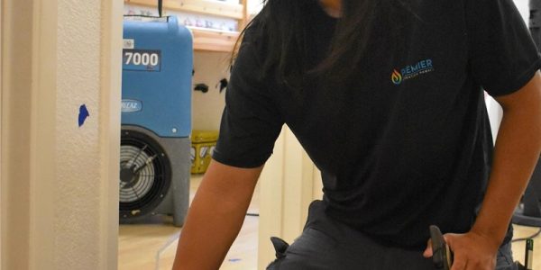 Technician using moisture meter during water damage restoration in home.