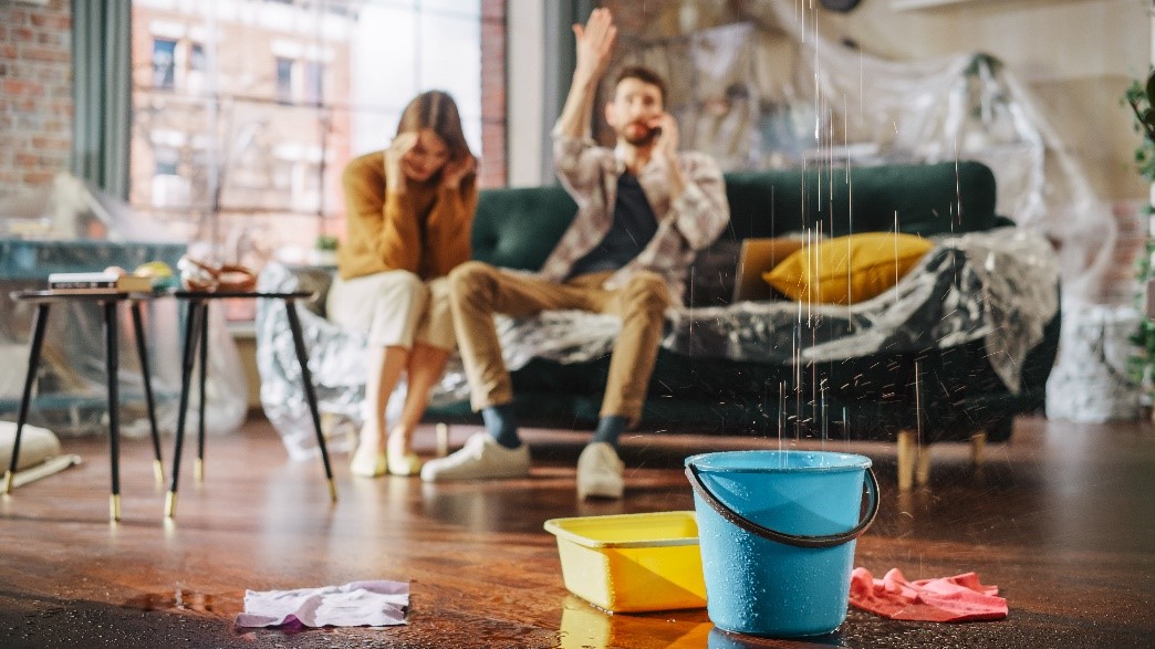 Living room with leaking ceiling, distressed couple, and buckets on floor.
