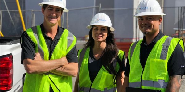 Three construction workers in safety vests and helmets at a building site.