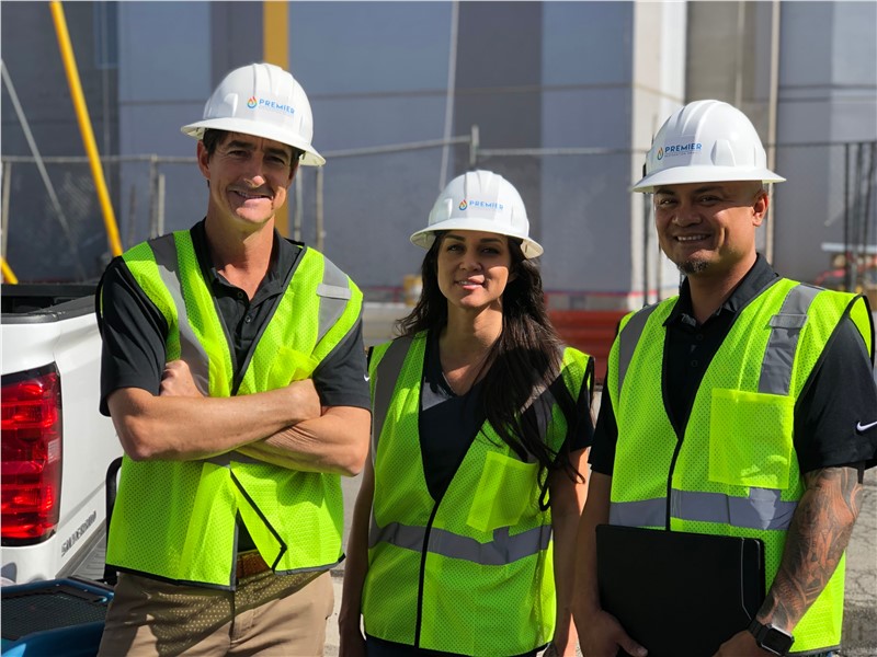 Three construction workers in safety vests and helmets at a building site.