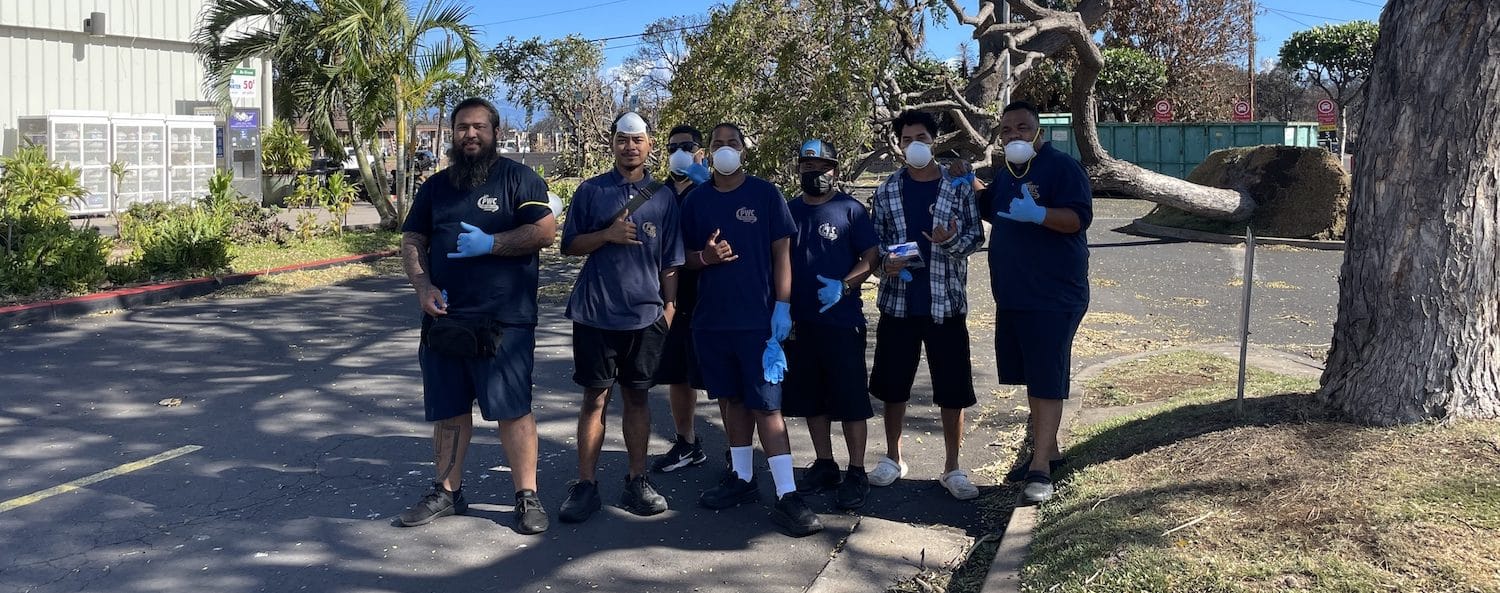 Group of workers wearing safety gear standing outdoors together near trees.
