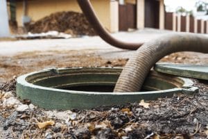 Sewage pump hose inserted into open ground-level drain access point during professional sewage extraction service.