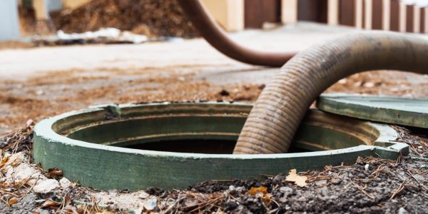 Sewage pump hose inserted into open ground-level drain access point during professional sewage extraction service.