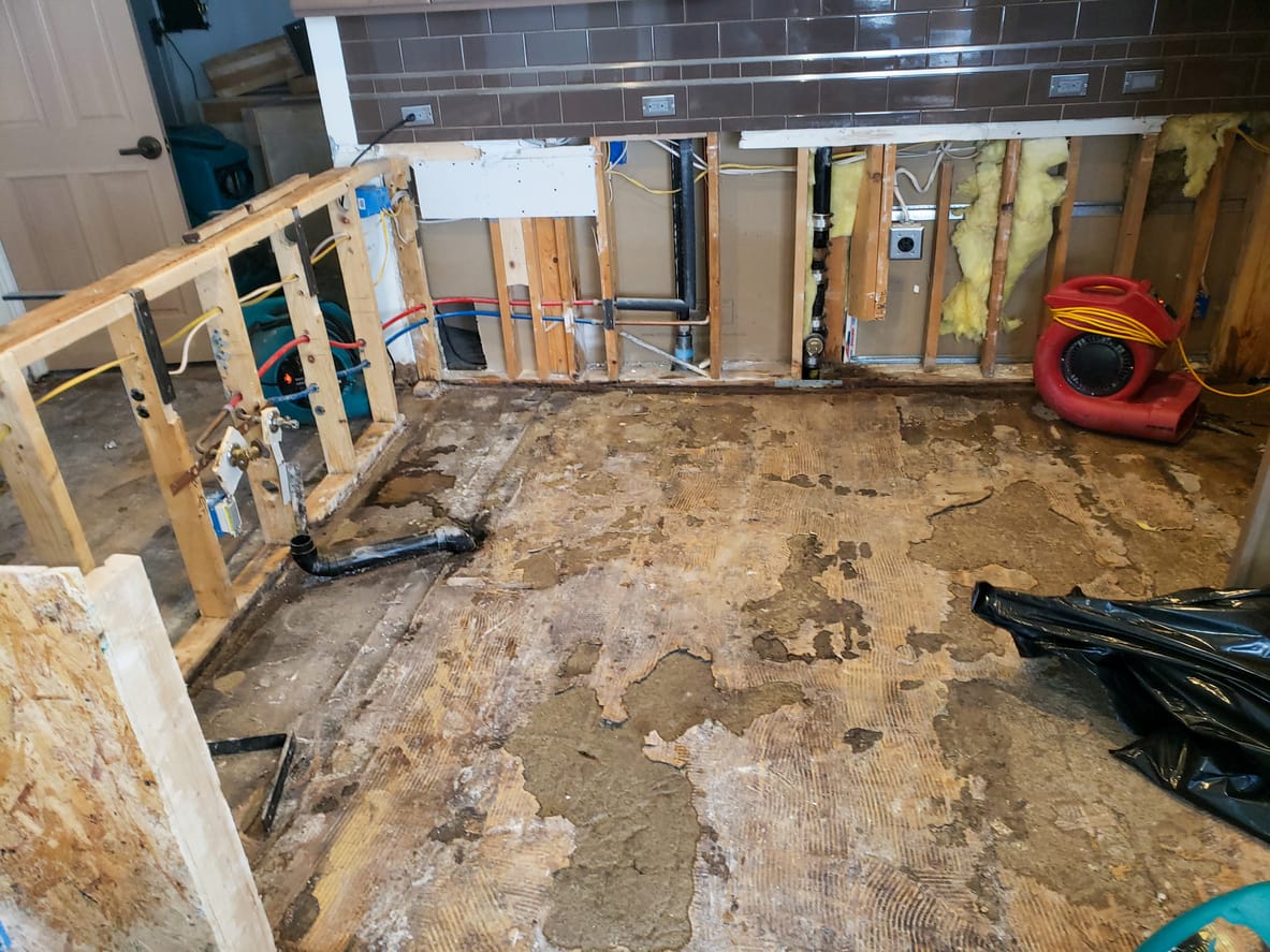 Hawaii water damage restoration in progress, exposed subfloor, wall studs, and industrial drying fans in a gutted kitchen.